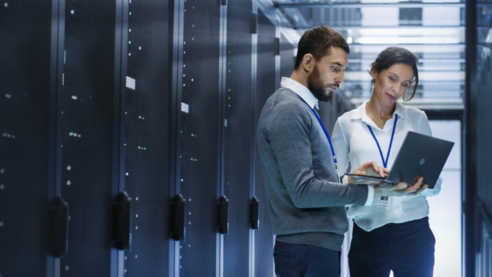 Male IT Specialist Holds Laptop and Discusses Work with Female Server Technician. They're Standing in Data Center, Rack Server Cabinet is Open.