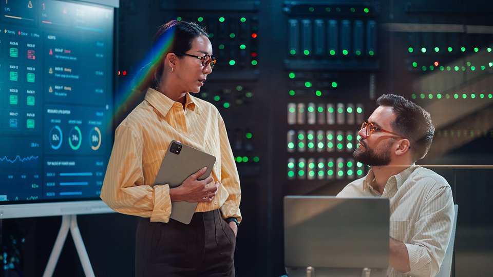 Information technology team collaborating in a server room, analyzing digital dashboard data for server management and system optimization