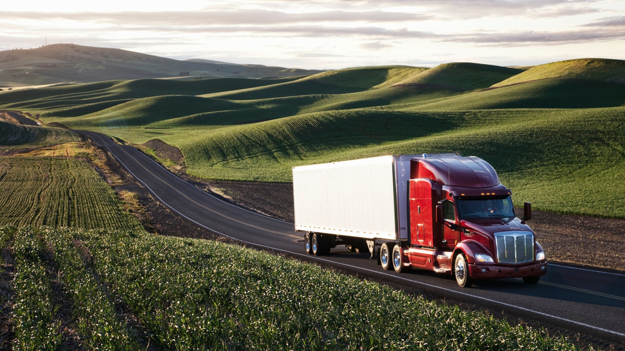 Peterbilt Class8 commercial truck driving through farmlands in eastern Washington, USA at sunset.
