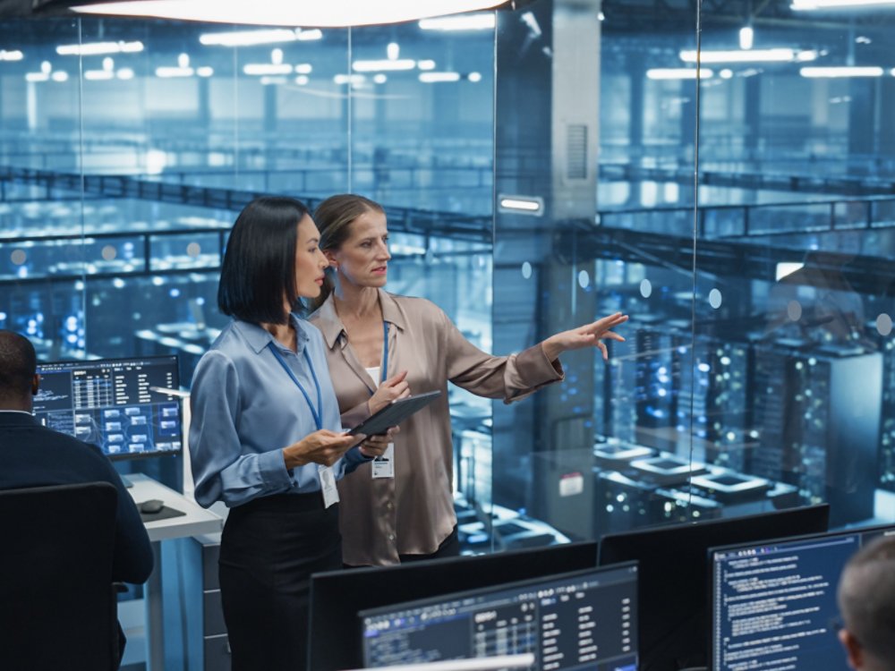 In a Modern Data Center, Caucasian Female Data Scientist and Asian Female AI Specialist Analyze Algorithms on a Tablet Computer. Specialists Exploring Optimizations for Processing Large Datasets
