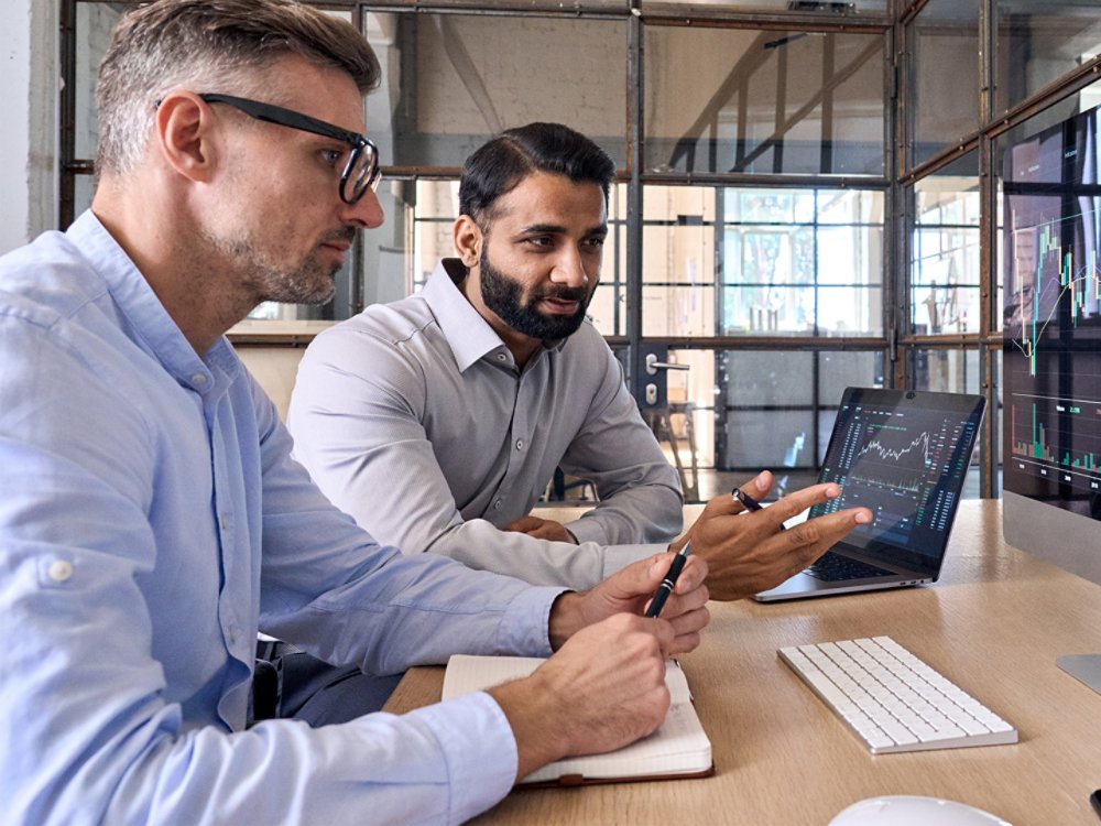 Two men in front of financial screen