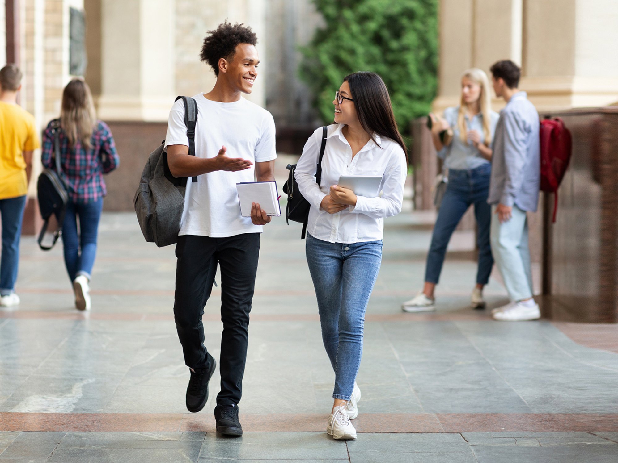 Happy diverse students walking in college campus during break and talking, copy space