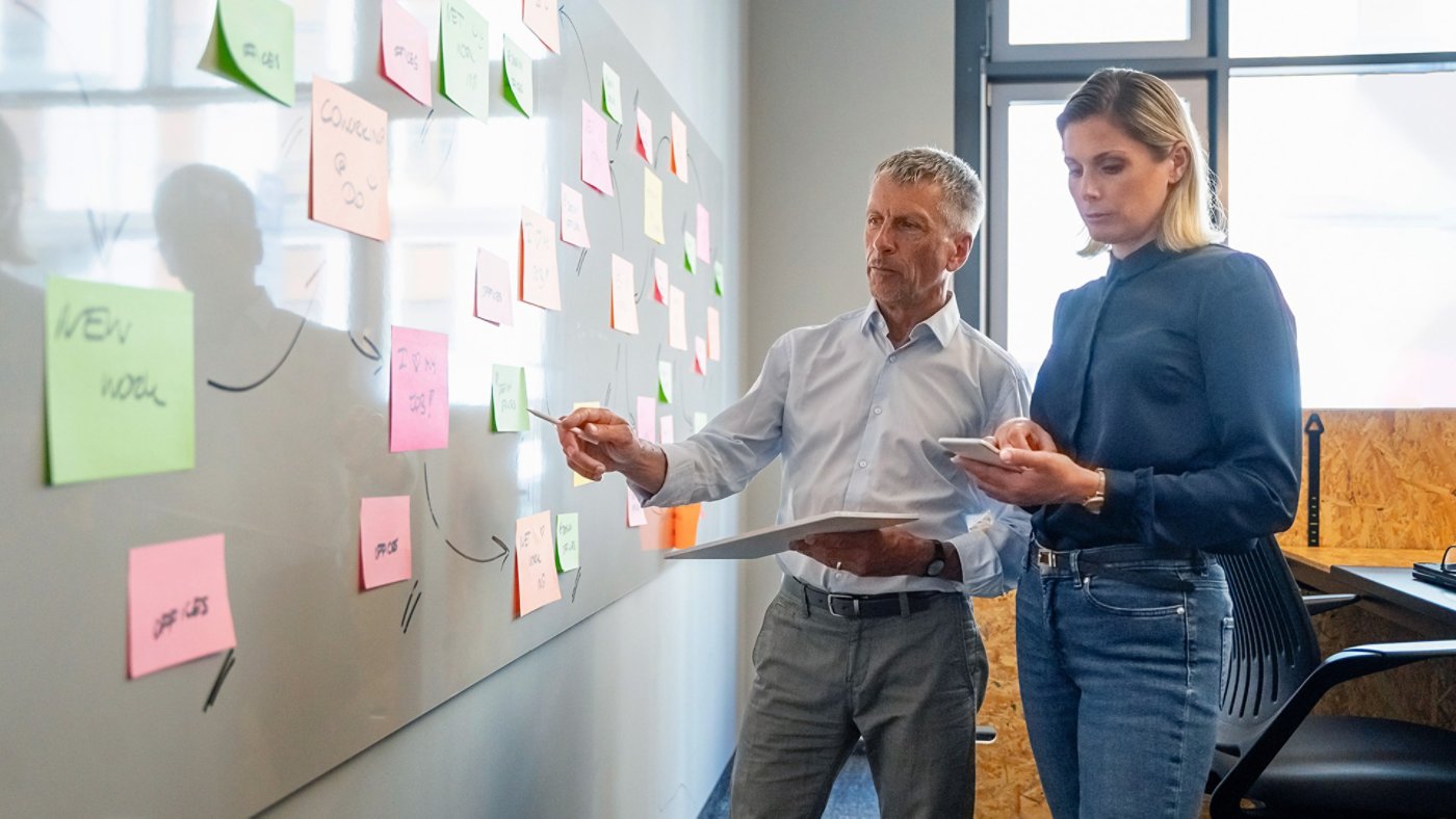 Senior businessman discussing over adhesive notes with colleague using smart phone in office