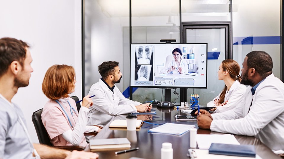 Large group of intercultural medical workers looking at their colleague on computer screen while watching online presentation