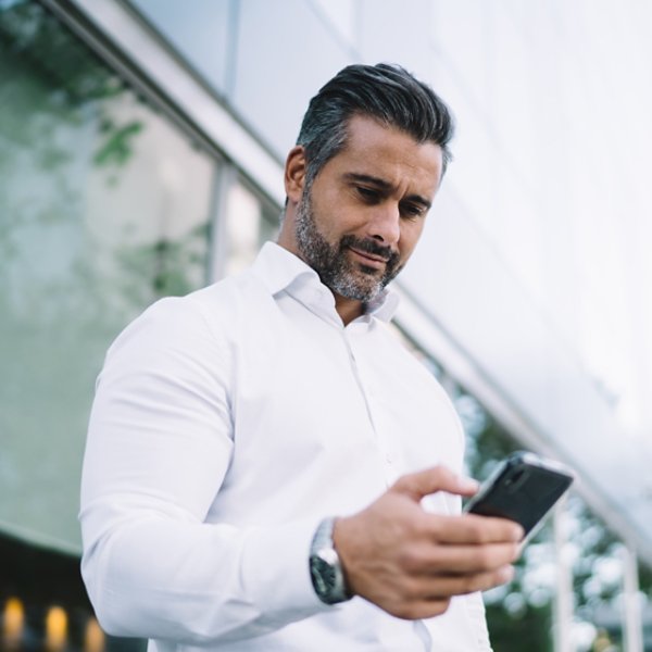 Below view of mature lawyer with stubble using mobile application for chatting in business chat, Caucasian male proud CEO in white shirt searching banking app for making online payment and banking