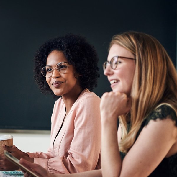 Two smiling businesswomen talking with colleagues during a meeting while sitting together at a boardroom table in a modern office