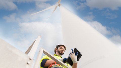 Male engineer working with plan inspecting or maintenance of wind turbines at windmill field farm. Male engineer using computer tablet control or monitoring wind turbine system at wind turbines farm