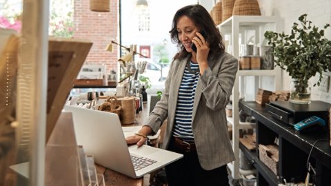 Woman on phone looking at laptop in store