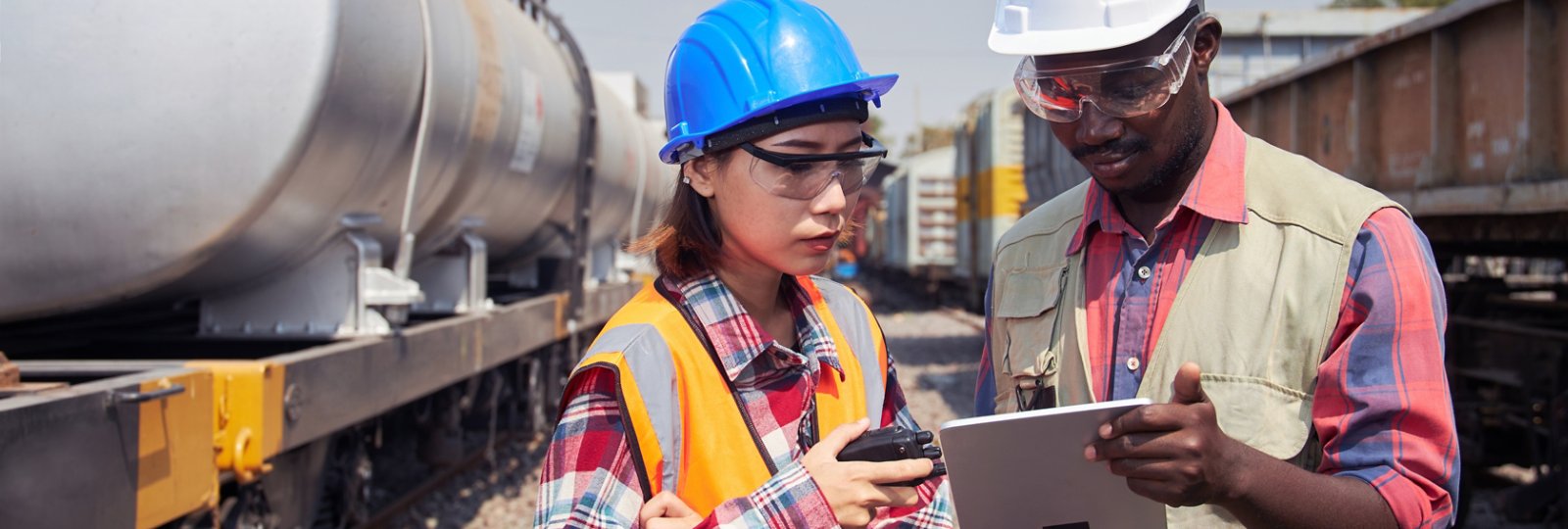 An engineer or technician, a freight train maintenance specialist, stands holding a tablet and is discussing outdoor maintenance work.