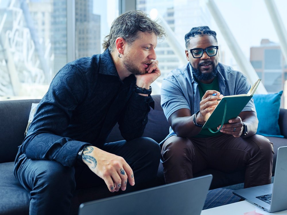 two guys collaborating with drawing pad on couch looking out over downtown