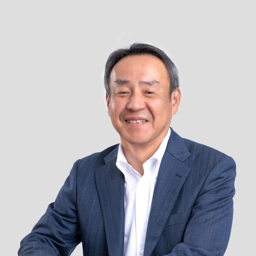 Portrait of a middle-aged man wearing a blue suit and white shirt. He is smiling warmly and looking slightly toward the camera. The background is a plain light grey, keeping the focus on the subject. The image has a clean, professional and approachable feel suitable for corporate or business use.