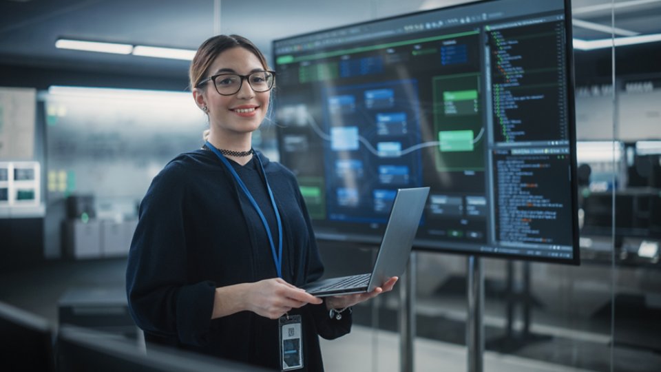 Portrait of a Beautiful Diverse Female Wearing Glasses, Using Laptop Computer, Looking at Camera and Smiling. Information Technology Specialist, Software Engineer or Developer