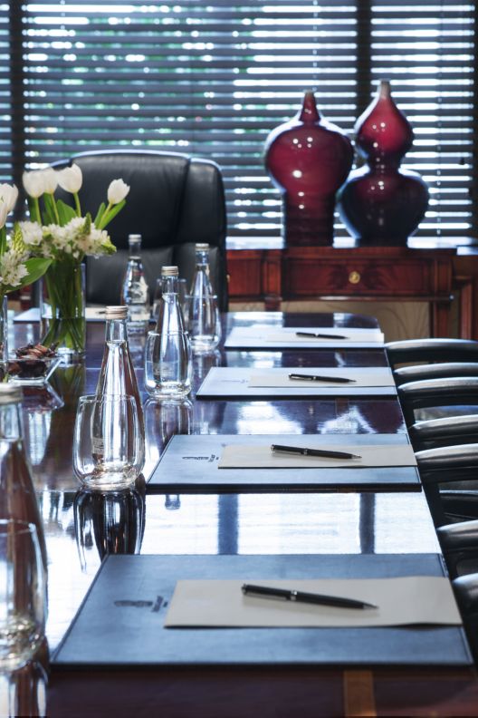 Executive chairs pulled up to conference table with floral arrangements and notepad settings.