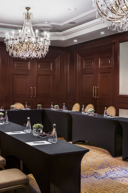 A U-shaped meeting table in a room with two large chandeliers and wood paneling