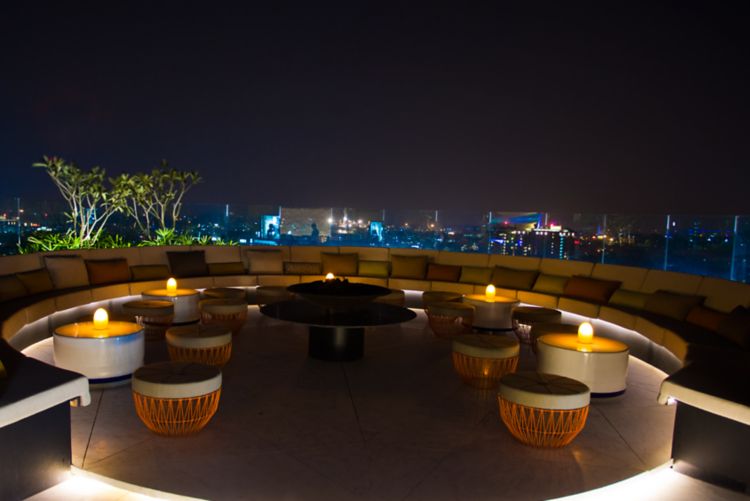 Circular rooftop bar with banquette seating, small round coffee tables and impressive skyline city views at night