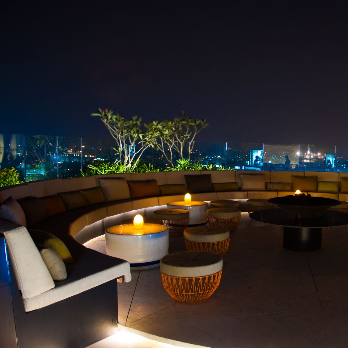 Circular rooftop bar with banquette seating, small round coffee tables and impressive skyline city views at night