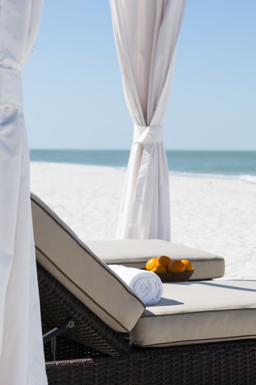 Two reclining chaise lounge chairs under the canopy of a private beach cabana.