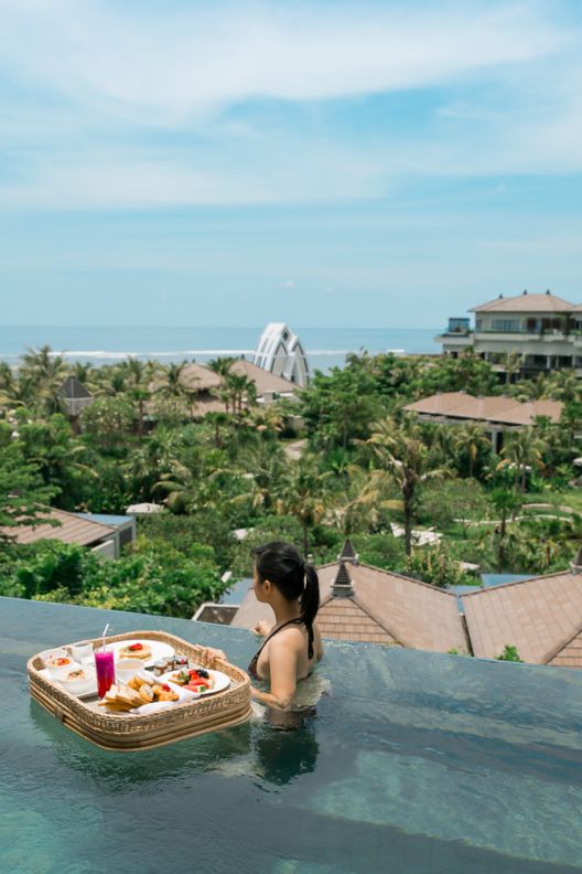 Woman in private villa pool enjoying floating breakfast.