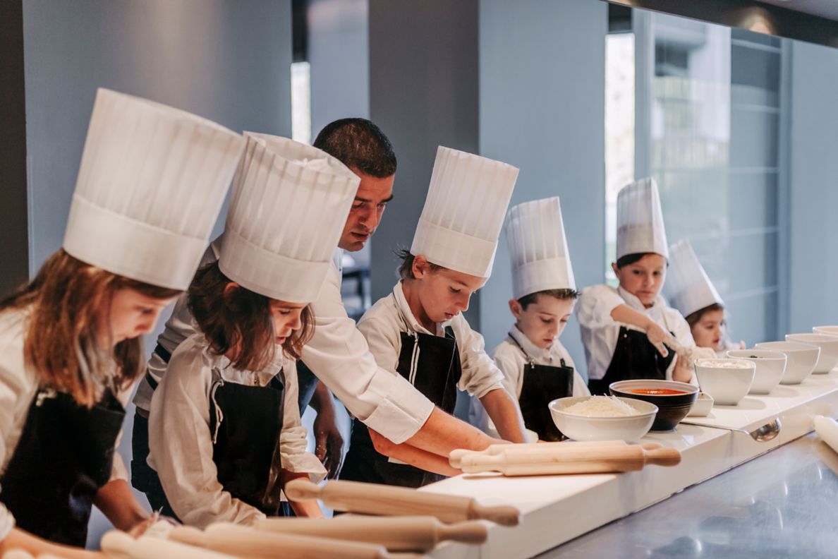 Children with chef's hats making pizza. 