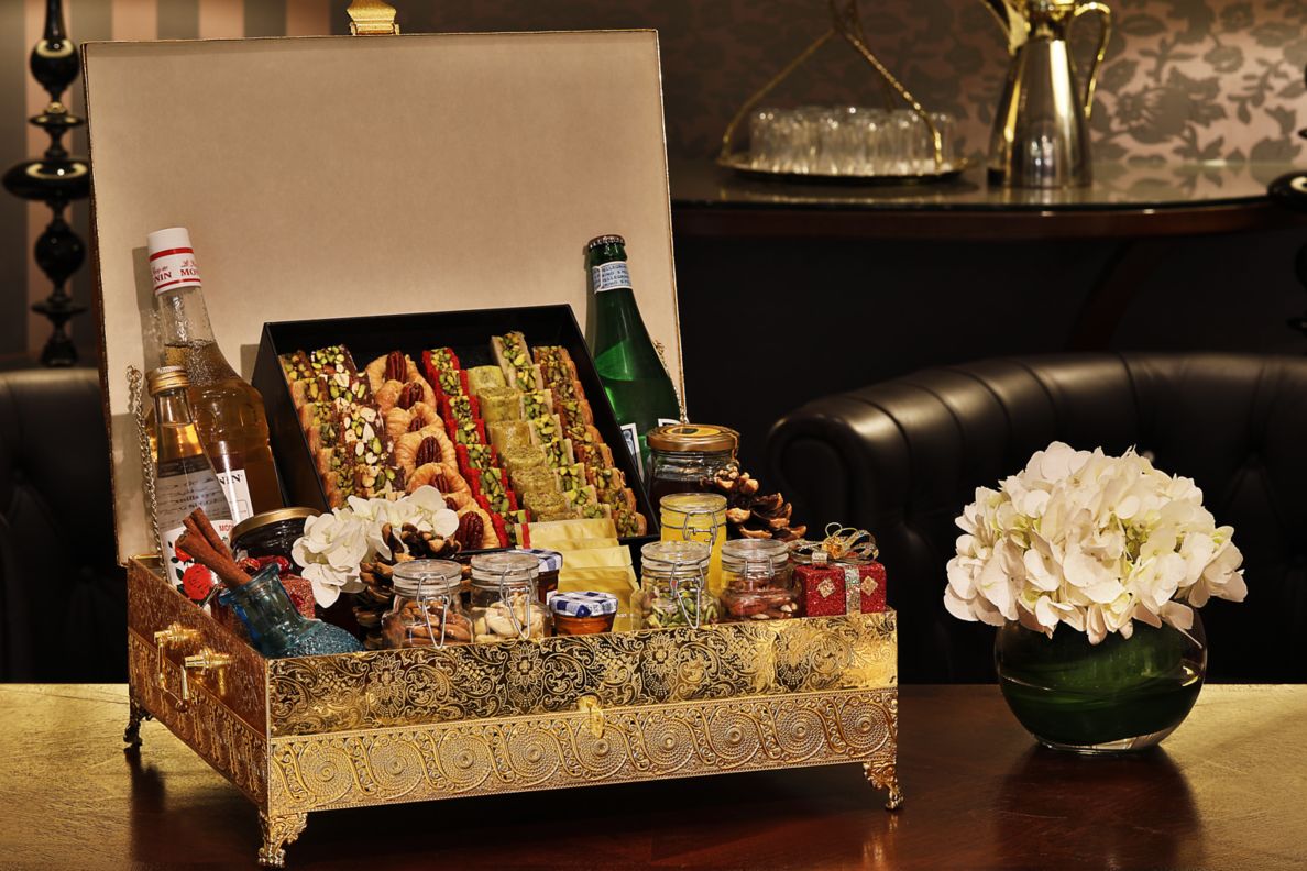 Wooden box filled with treats, candies, nuts, and sparkling water next to a vase of flowers. 