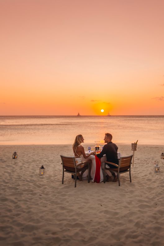 Couple sitting on beach.at table with glasses of wine.