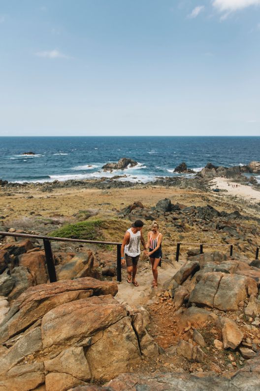 Couple walking up rocky cliff with ocean in the background. 