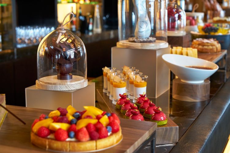 Counter laden with fruit tarts, pastries and confections as well as chocolate sculptures encased in glass domes