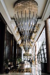 A large black and gold chandelier hangs in a hotel lobby.