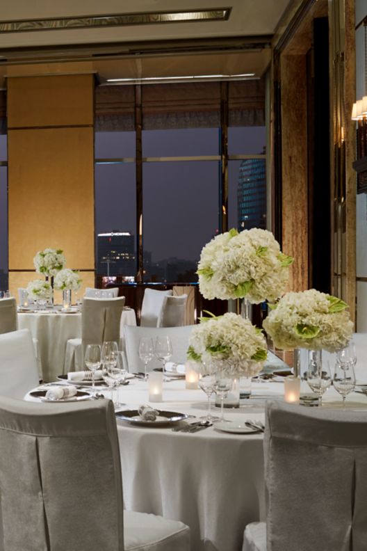 beige ballroom - banquet setup with round tables  and silverware on the top with floral decorations.