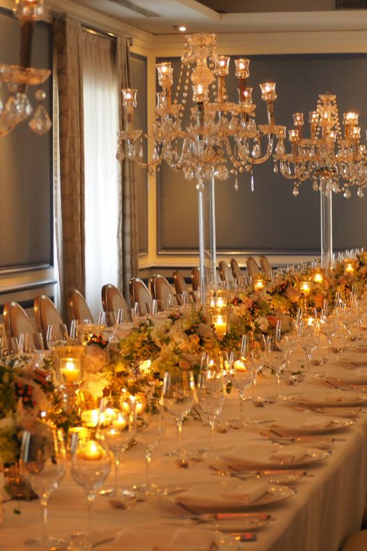 Long reception dining table with mini chandelier table placements, candles, floral decorations and silverware.