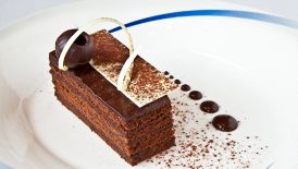 A rectangular piece of chocolate layer cake with an artistic topping in white and dark chocolate