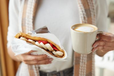 Person holding cup of coffee and stuffed crepe