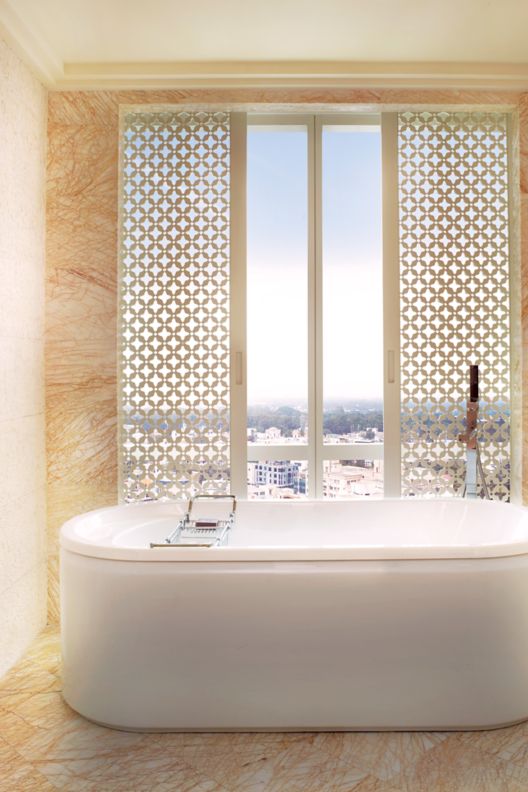 Freestanding  white tub in a peach marble bathroom with floor-to-ceiling windows overlooking the skyline