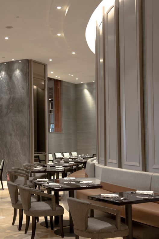 Modern restaurant seating with a chocolate banquette lining a wall while tables and sleek gray chairs are positioned opposite