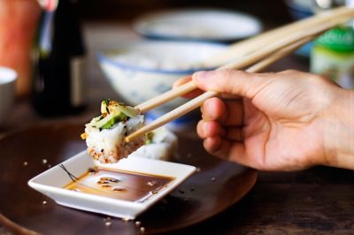 Hand holding chopsticks with piece of sushi