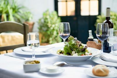 A fine dining table with a white tablecloth, plates of food, and a glass of wine