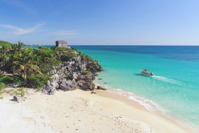 Stone temple ruins next to a white-sand beach and blue sea