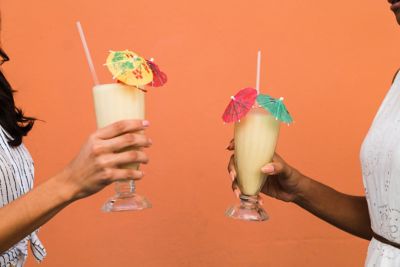 Two women drink pi�a coladas in front of a colorful wall