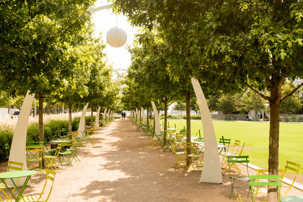 A path lined with small tables and chairs and overlooked by trees