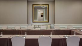U-shaped meeting table beneath a chandelier with a wall mirror reflecting a framed painting in the hallway
