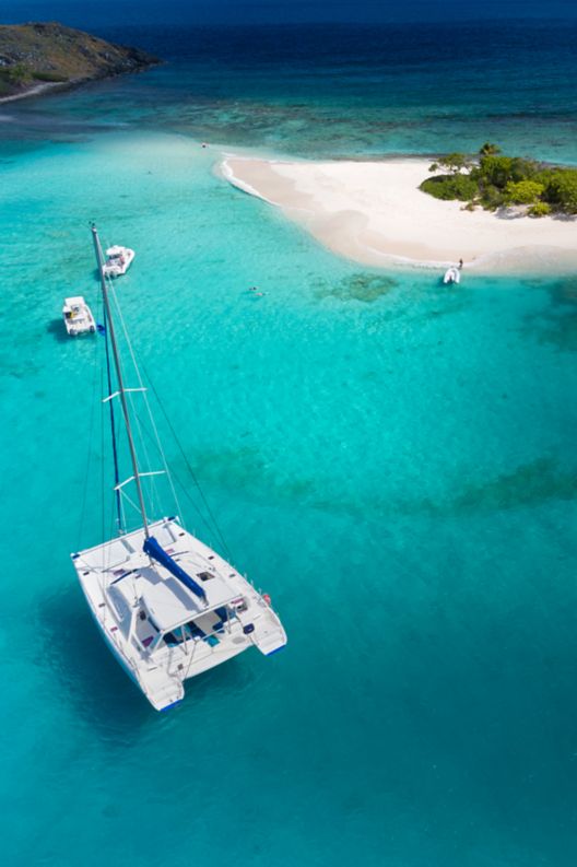  Catamaran boat parked next to a small sandy island. 
