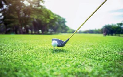 A golf club lines up to a ball on a tee