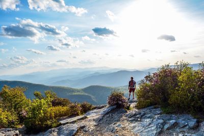 A man hiking on a rock ledge and looking at the sun