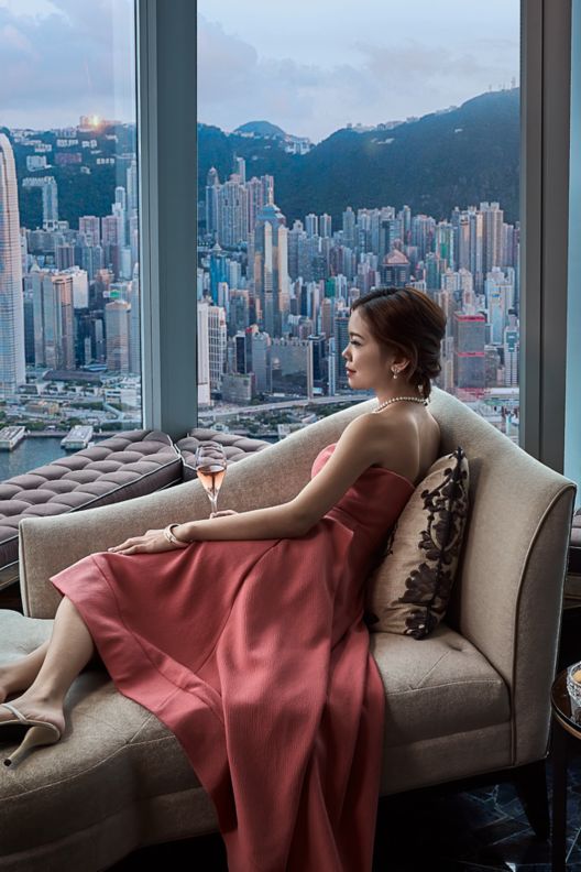 Lady sitting next to the window with view of the Hong Kong skyline beyond.
