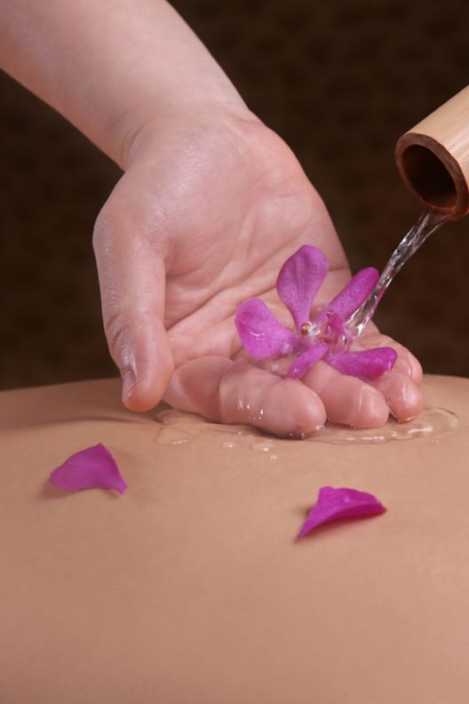 Oil and flower petals are used to prepare for a back massage