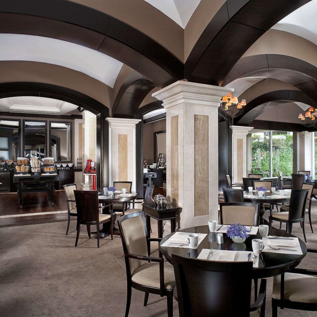 An elegant dining room with arched ceilings, columns, a buffet area and floor-to-ceiling windows
