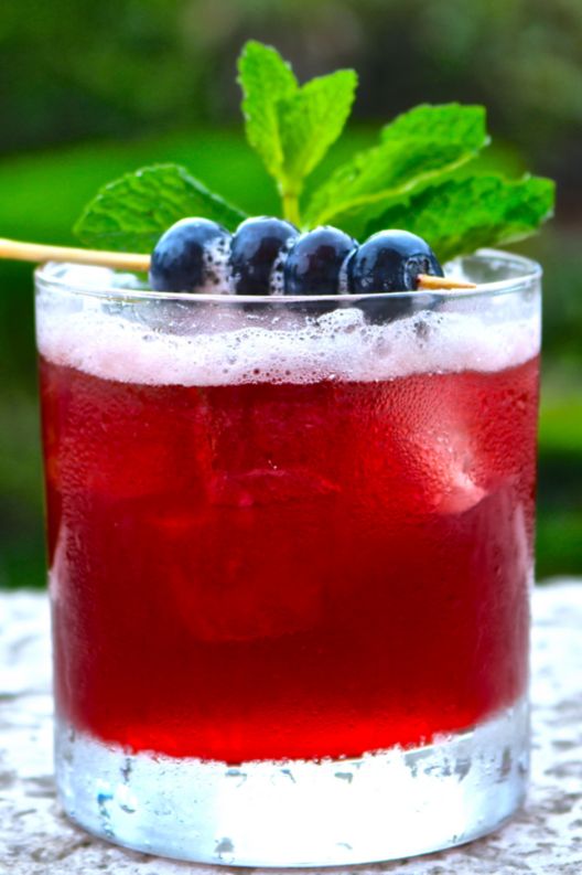 A cocktail with berries and mint leaves on top.