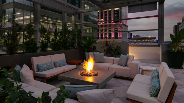Soft padded outdoor sectional sofa seating surrounding a flaming, modern, tabletop firepit at dusk