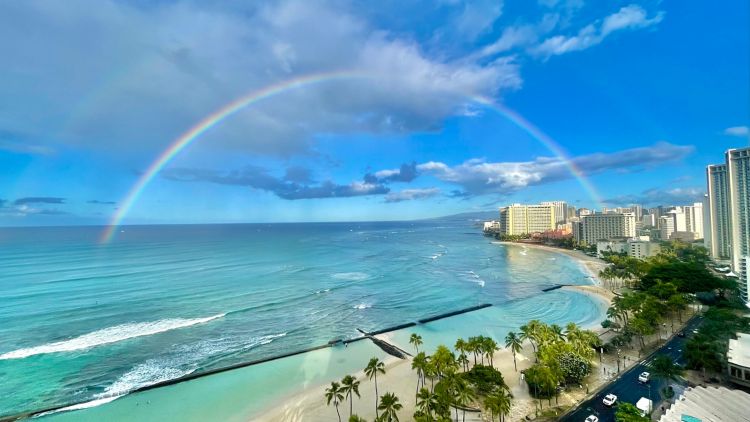 A rainbow arched over ocean and buildings along the shore.