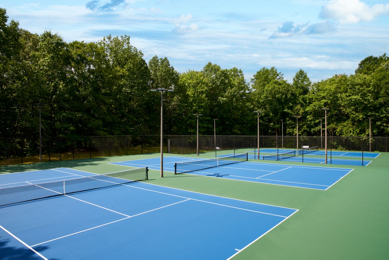 Six outdoor tennis courts surrounded by lush trees